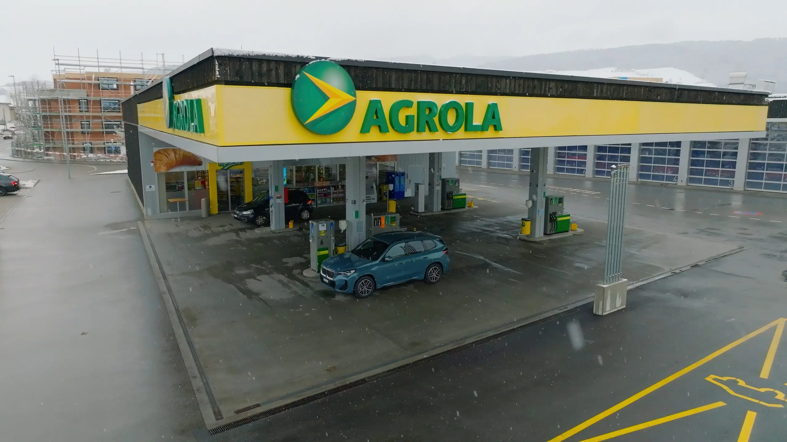 Agrola-Tankstelle mit Zapfsäulen und Autos auf nassem Gelände bei Schneefall