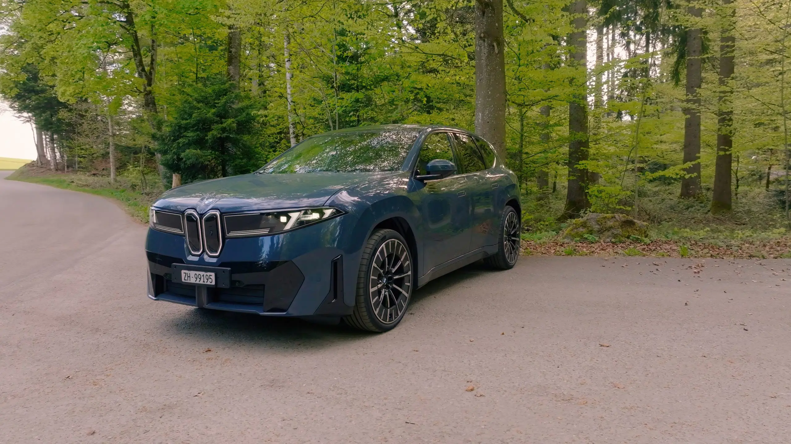 Blauer BMW iX3 steht auf einer Waldstrasse, als Premium-Konkurrent zum Zeekr 7X.