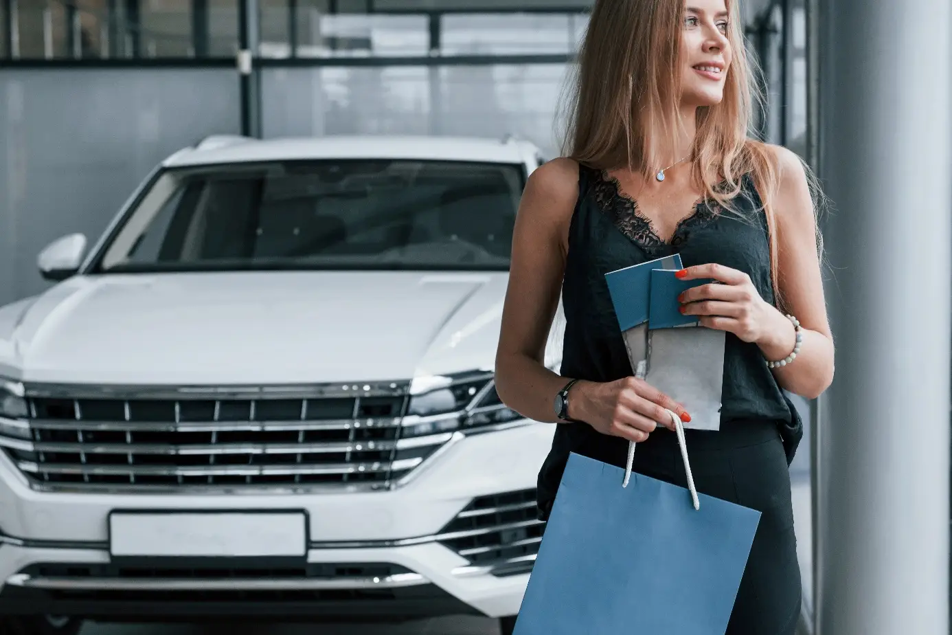 Frau im Autohaus vor einem weissen Neuwagen, mit Unterlagen in der Hand.