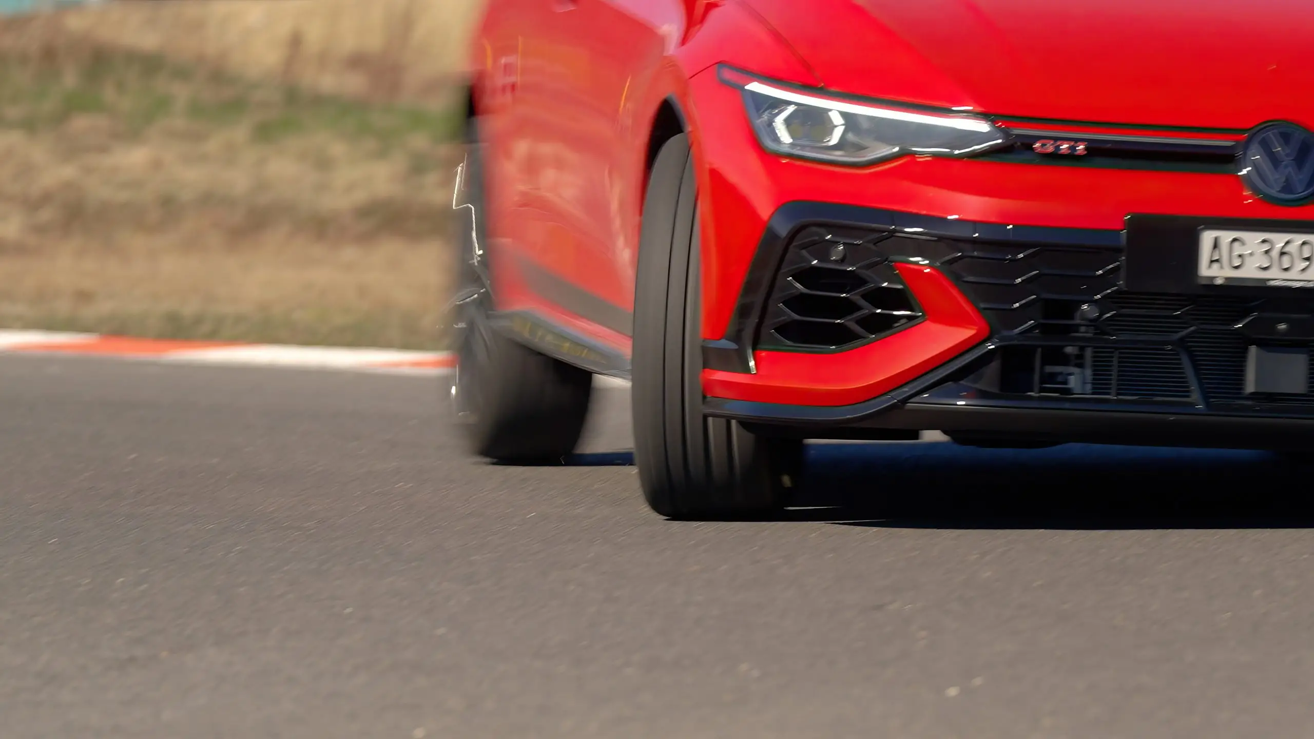 Roter VW Golf GTI fährt auf der Teststrecke durch eine Kurve, Vorderreifen haften sichtbar auf dem Asphalt.