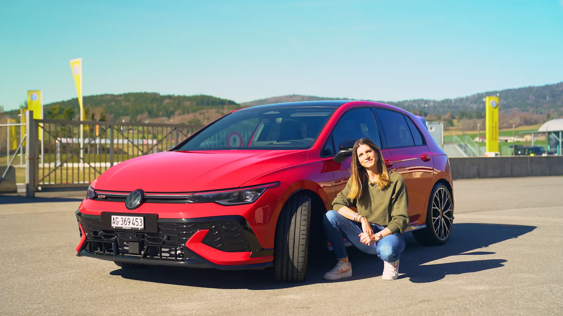 Cyndie Allemann kniet neben einem roten VW Golf GTI auf der Teststrecke in Lignières.