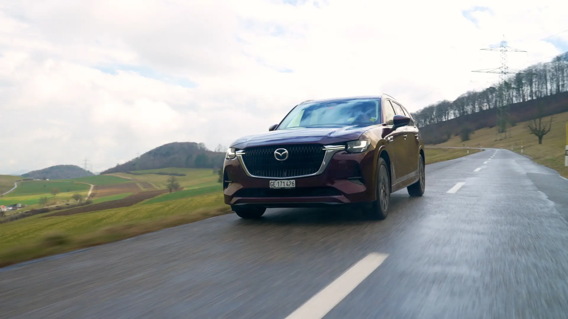 Dunkler Diesel-SUV fährt auf nasser Landstrasse durch eine hügelige Landschaft.