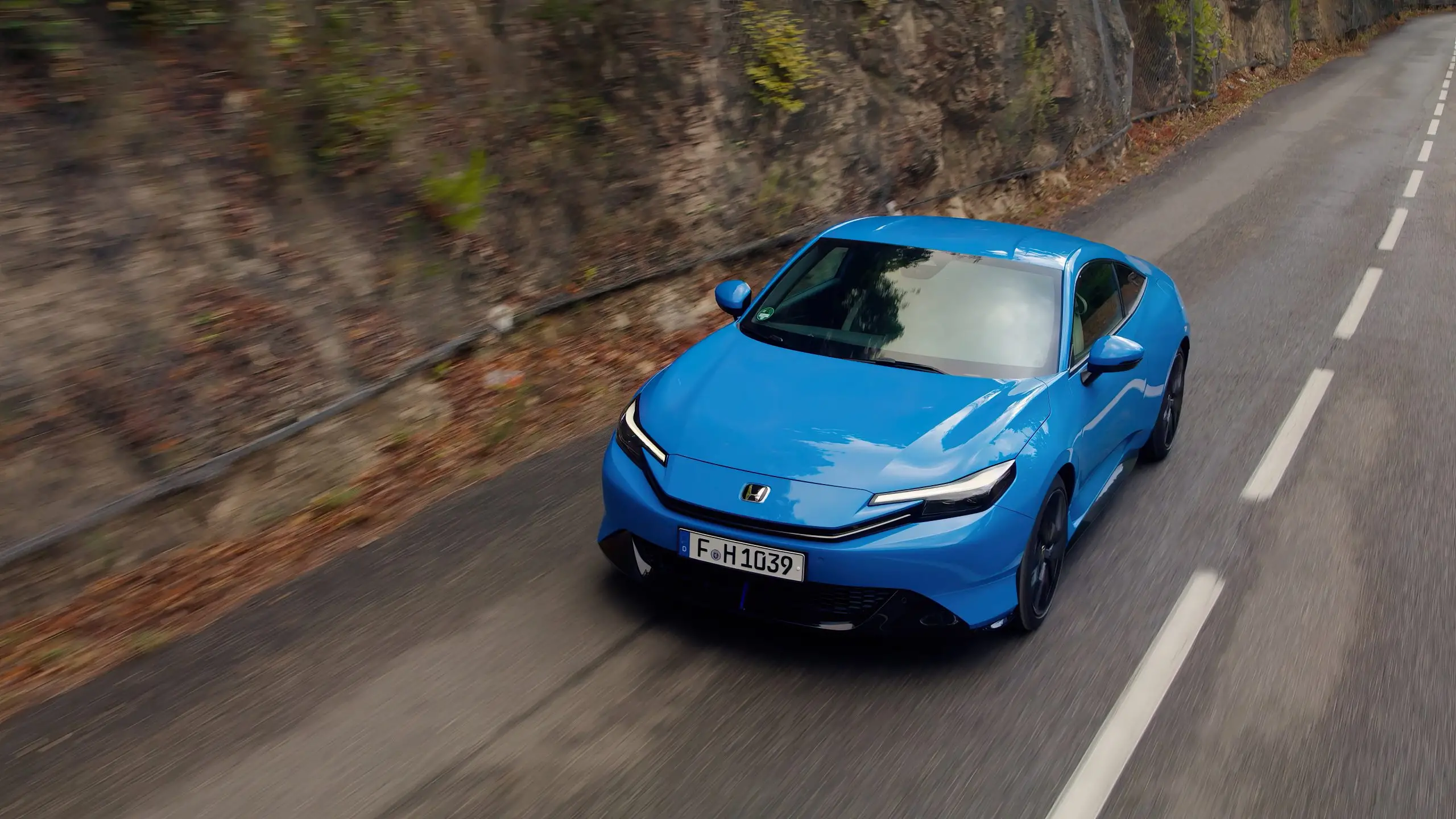 Blauer Honda Prelude fährt auf einer kurvigen Landstrasse durch felsiges Waldgebiet