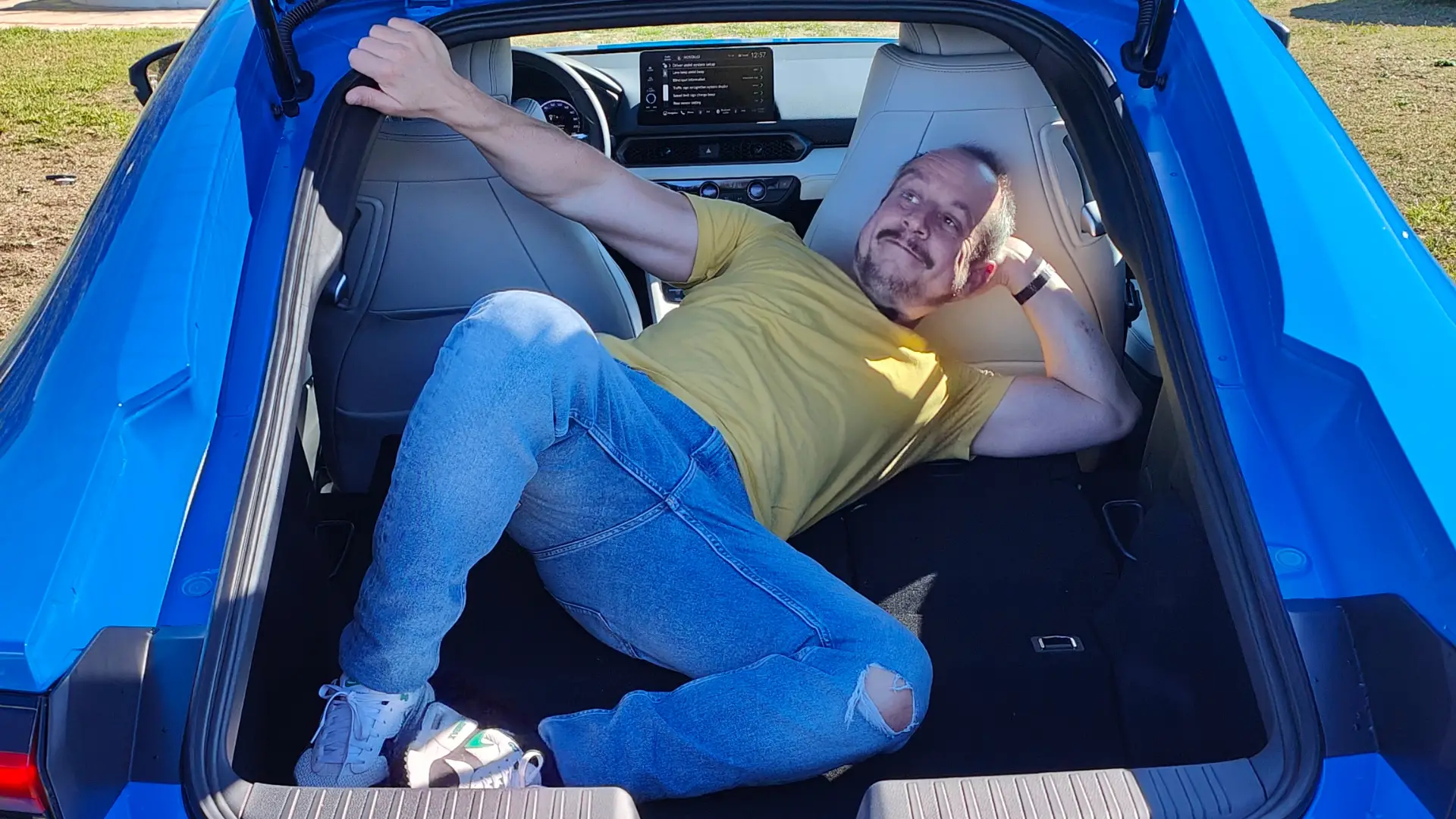 Sämi liegt im geöffneten Laderaum des blauen Honda Prelude und demonstriert das Platzangebot.