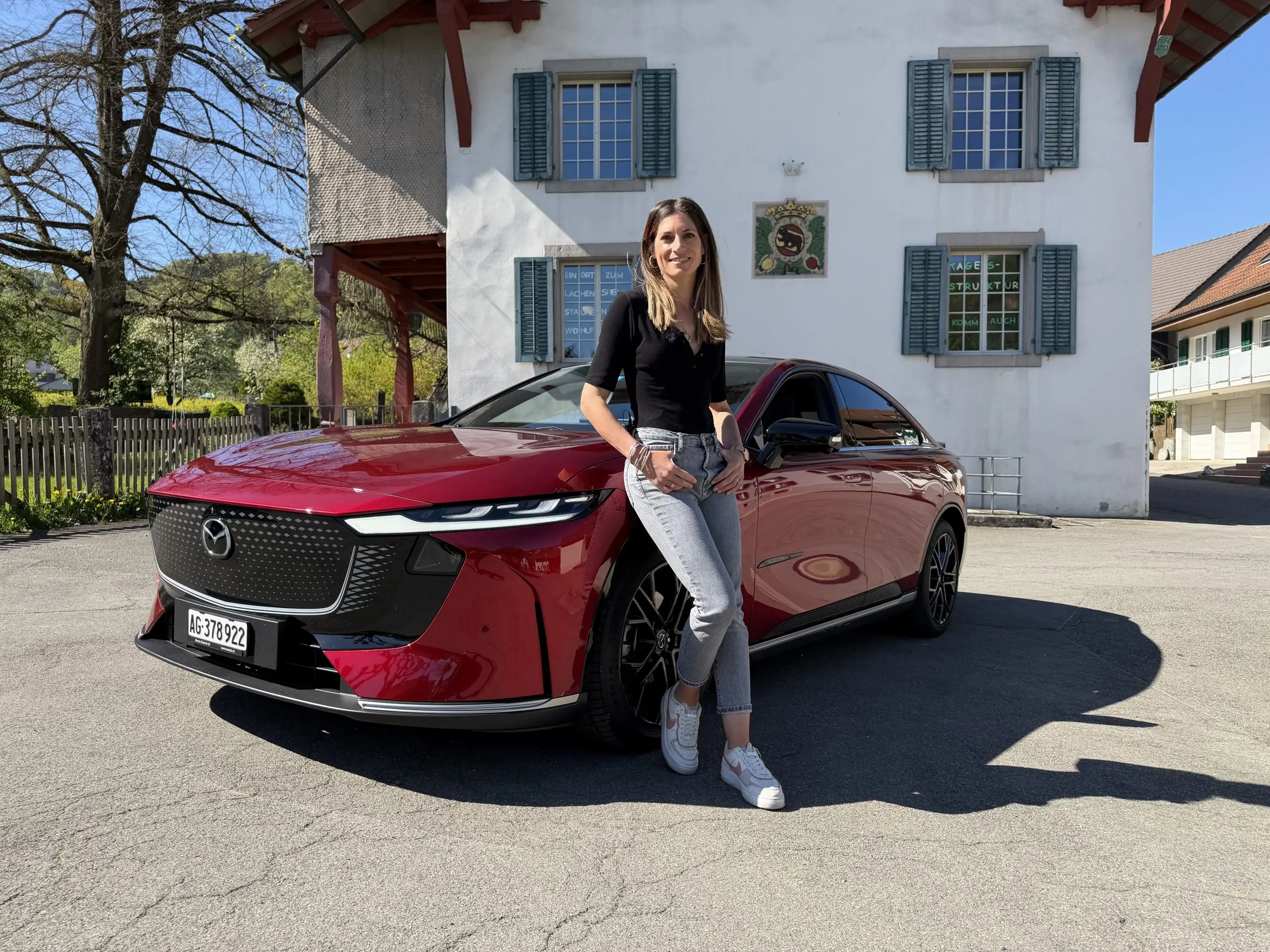 Cyndie Allemann lehnt an einem roten Mazda 6e vor einem Gebäude mit grünen Fensterläden.