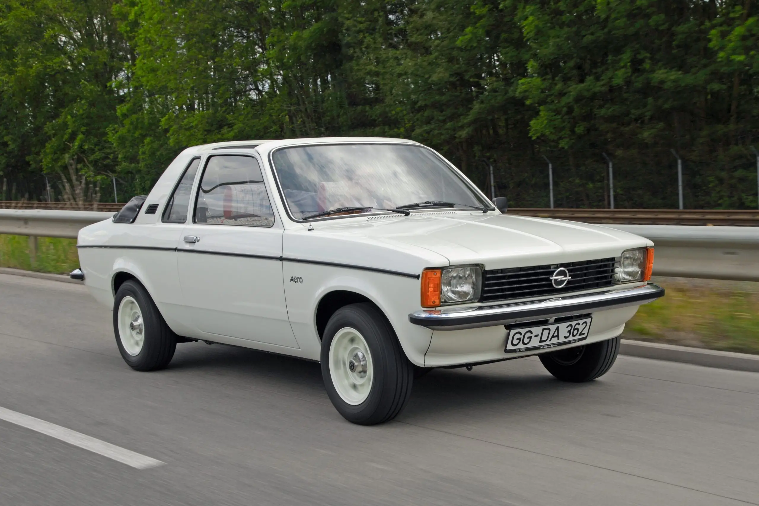 Weisser Opel Kadett aus den 1970ern fährt auf einer Strasse.