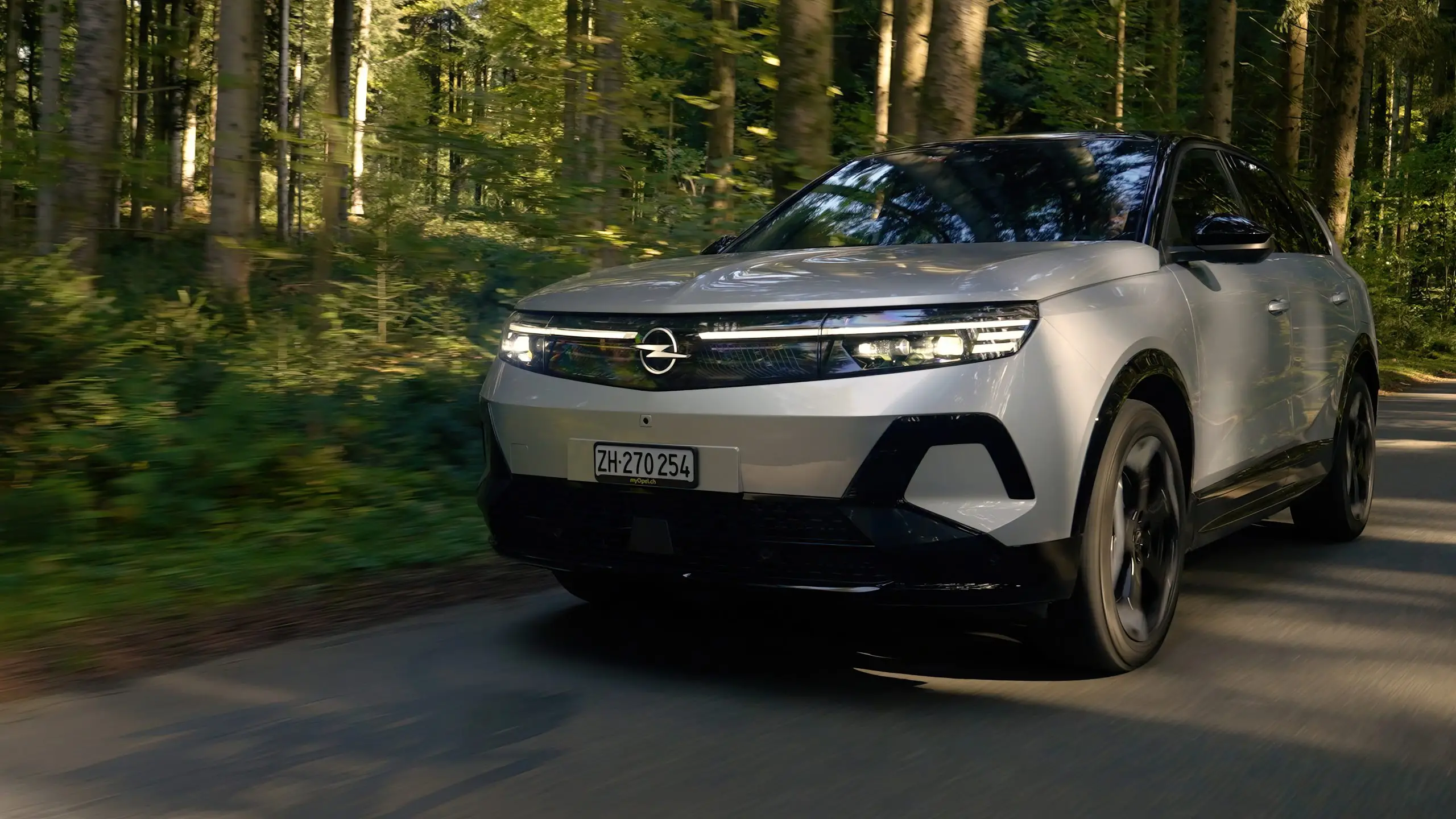 Weisser Opel Grandland fährt auf einer Waldstrasse, Front und Scheinwerfer im Fokus.