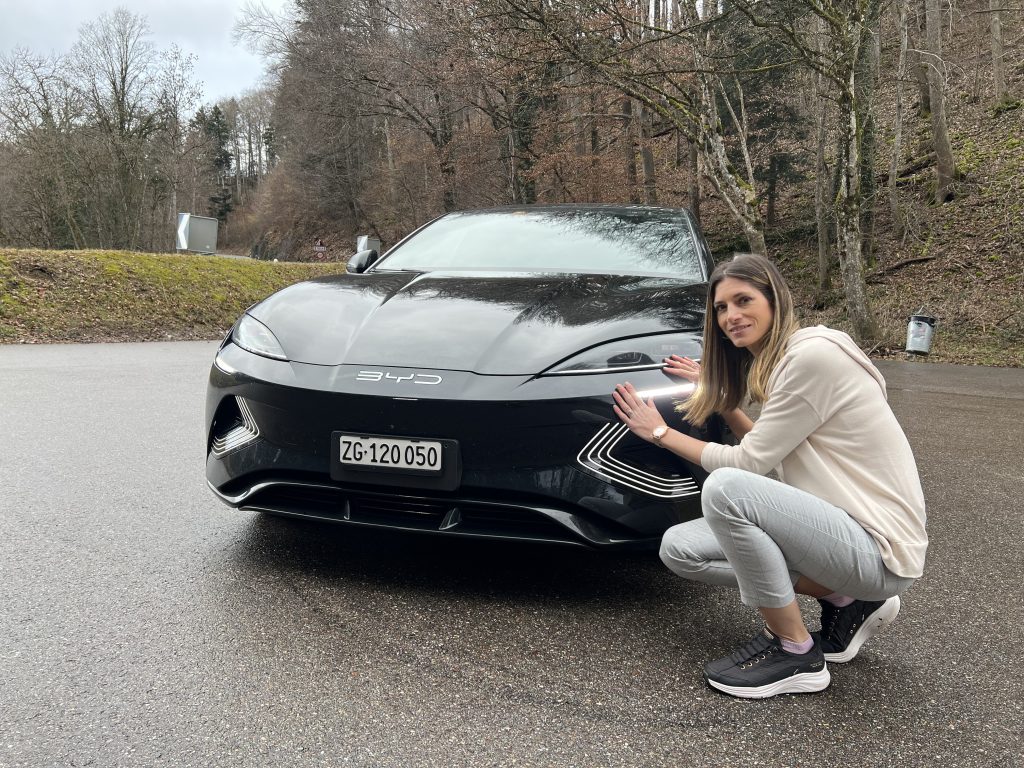 Schwarzer BYD Seal von vorne auf nasser Strasse, daneben kniet die Testerin.