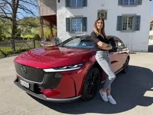 Frau lehnt vor einem hellen Haus an einem roten Mazda 6e.