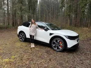 Cyndie Allemann steht neben einem weissen Zeekr 7X auf einem Waldweg.