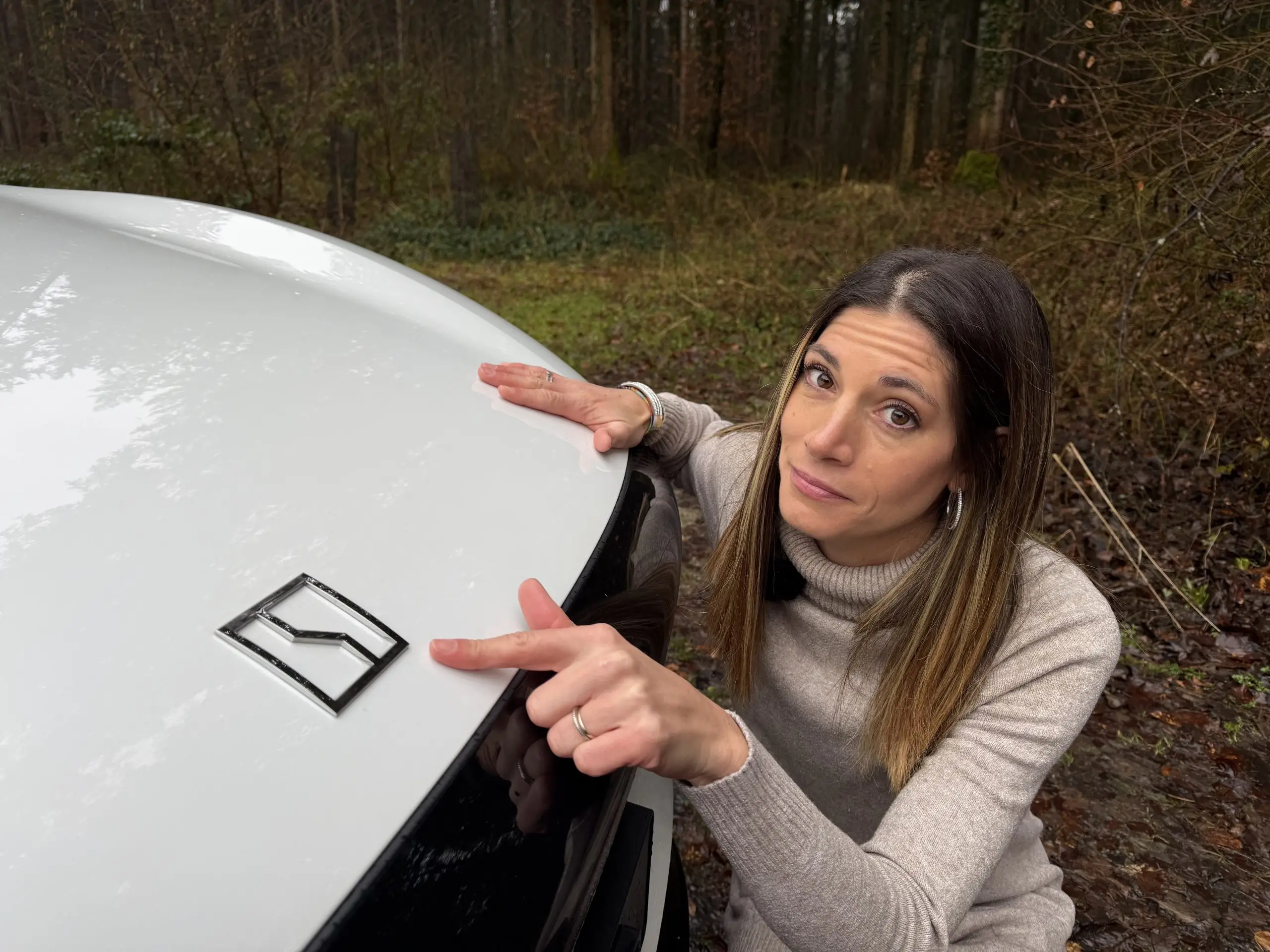 Cyndie Allemann zeigt auf das Zeekr-Logo an der Front eines weissen 7X im Wald.