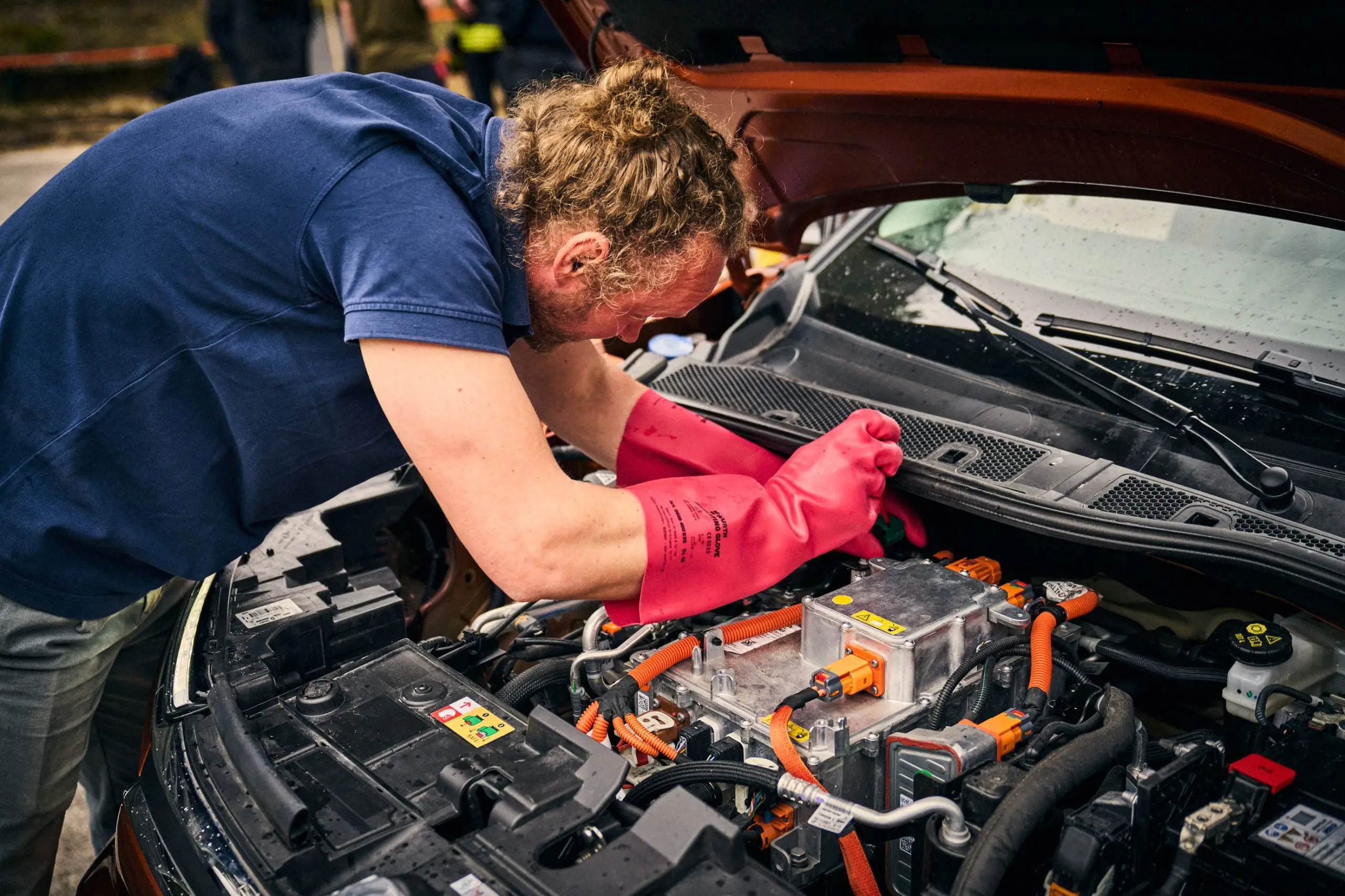 Experte prüft mit roten Schutzhandschuhen die Hochvolt-Komponenten eines Elektroautos nach dem Wassertest