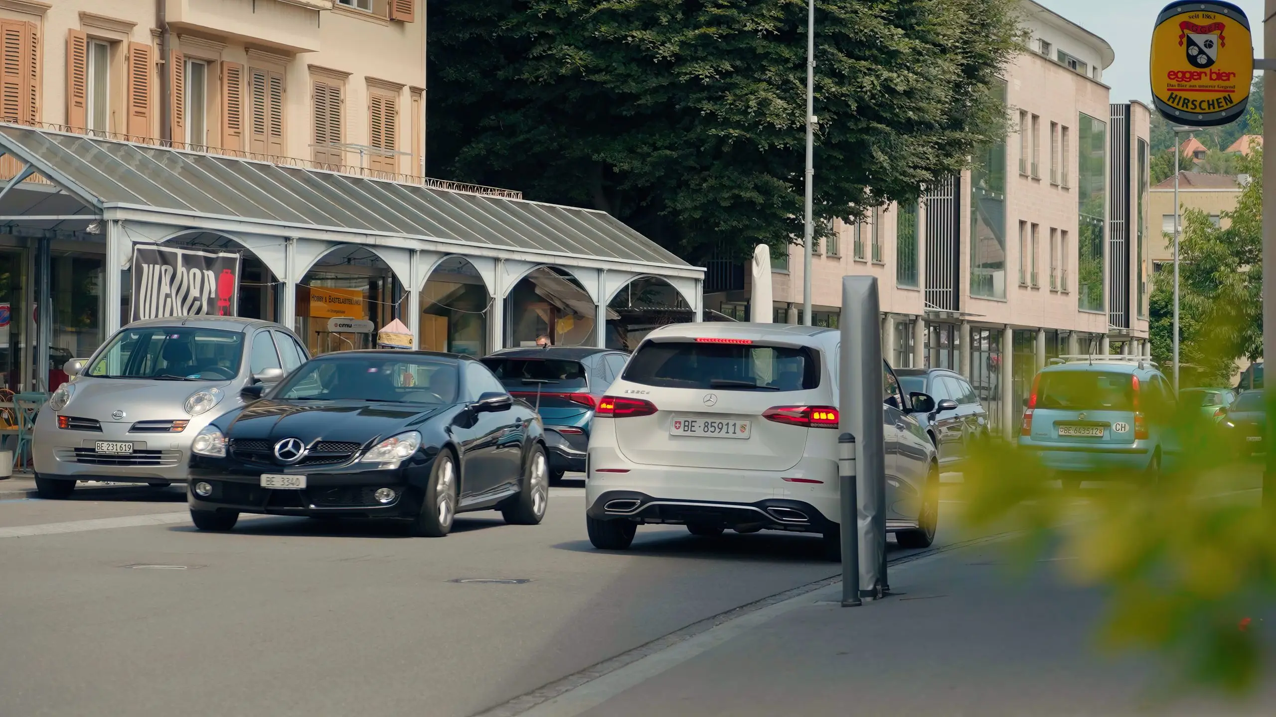 Mehrere Autos fahren durch eine belebte Stadtstrasse an Häusern und Geschäften vorbei.