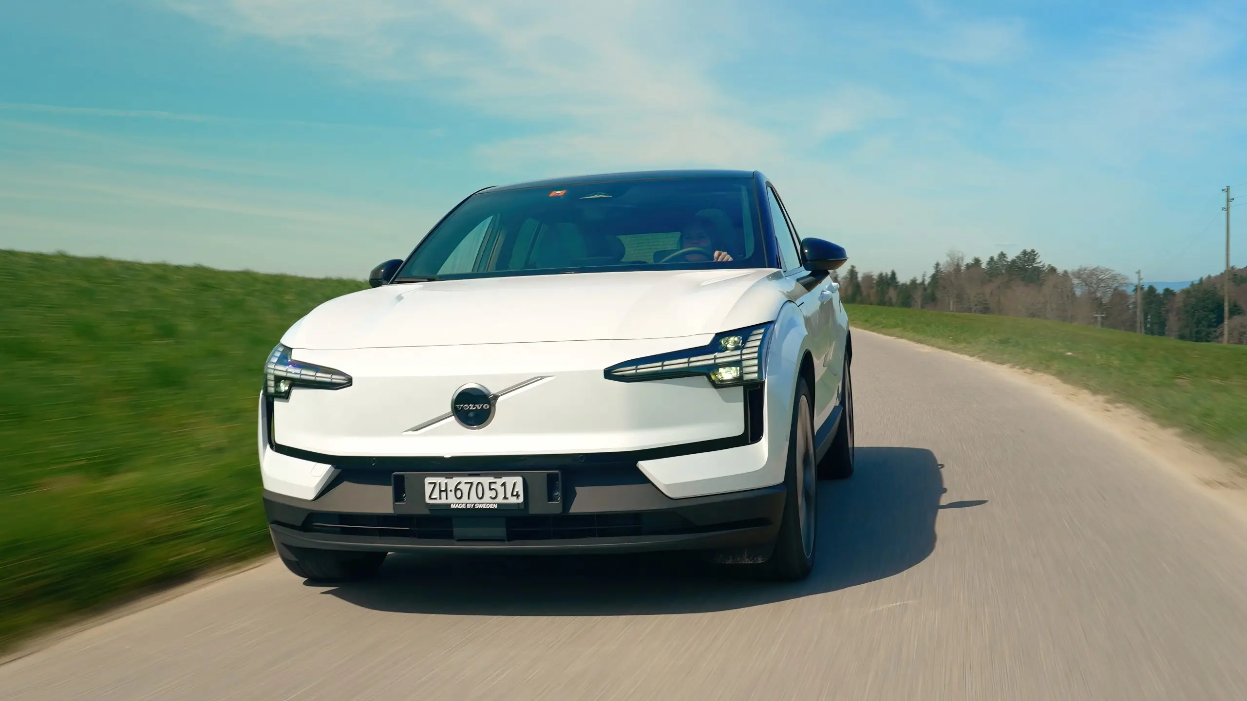 Weisses Elektroauto fährt auf einer Landstrasse, im Fokus der Vergleich von Motor- und Reifengeräuschen.