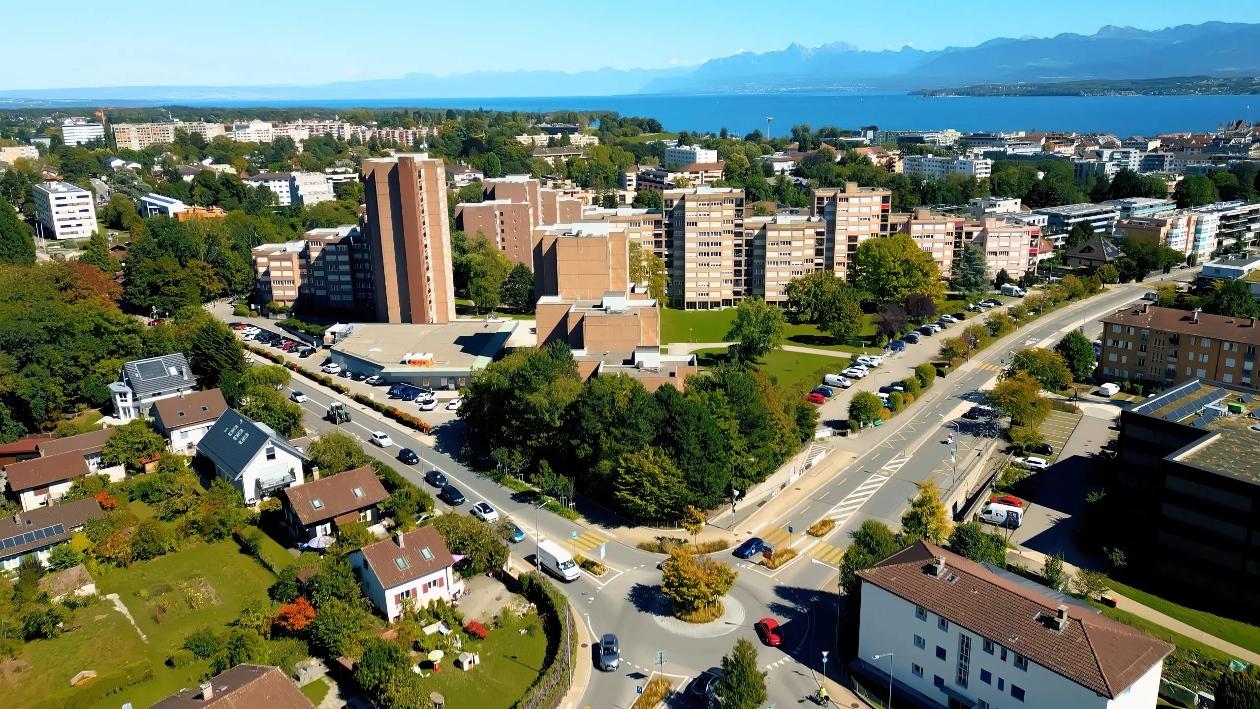 Städtisches Wohnquartier mit viel befahrener Kreuzung, im Hintergrund See und Berge.