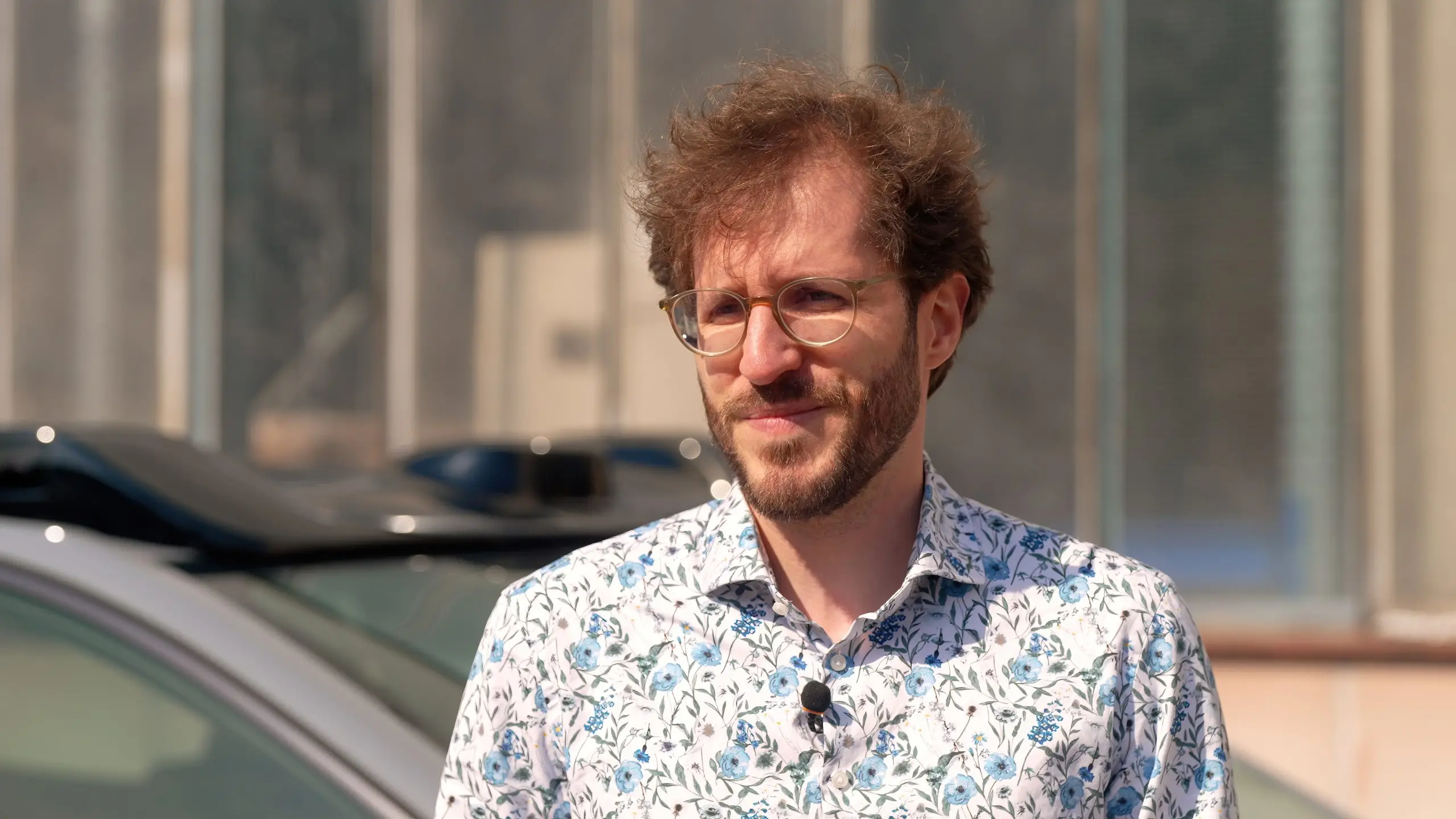 Julian Renninger steht mit Mikrofon vor einem Testfahrzeug für automatisiertes Fahren.