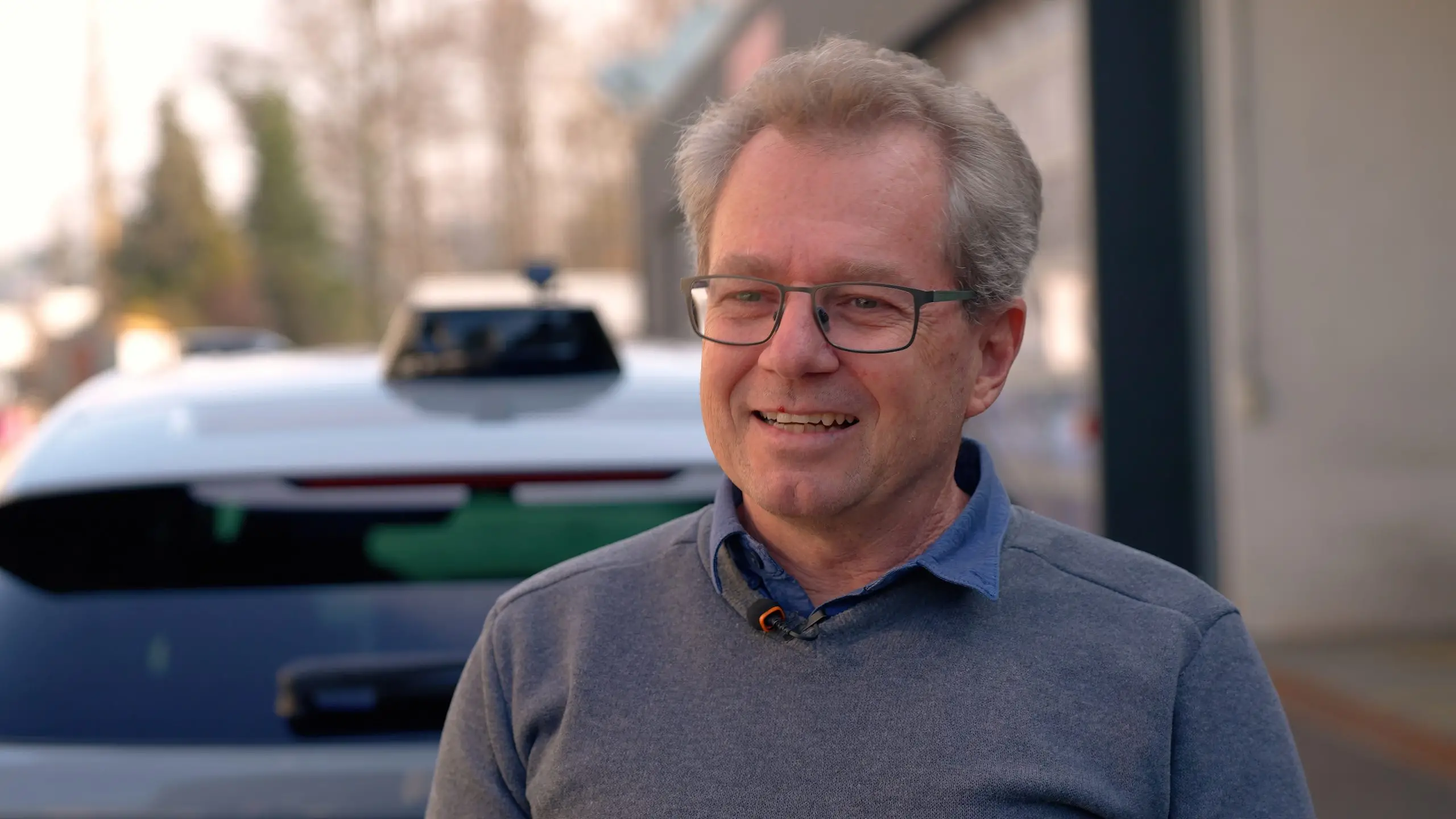Raphael Murri steht lächelnd vor dem automatisierten Testfahrzeug in Regensdorf.