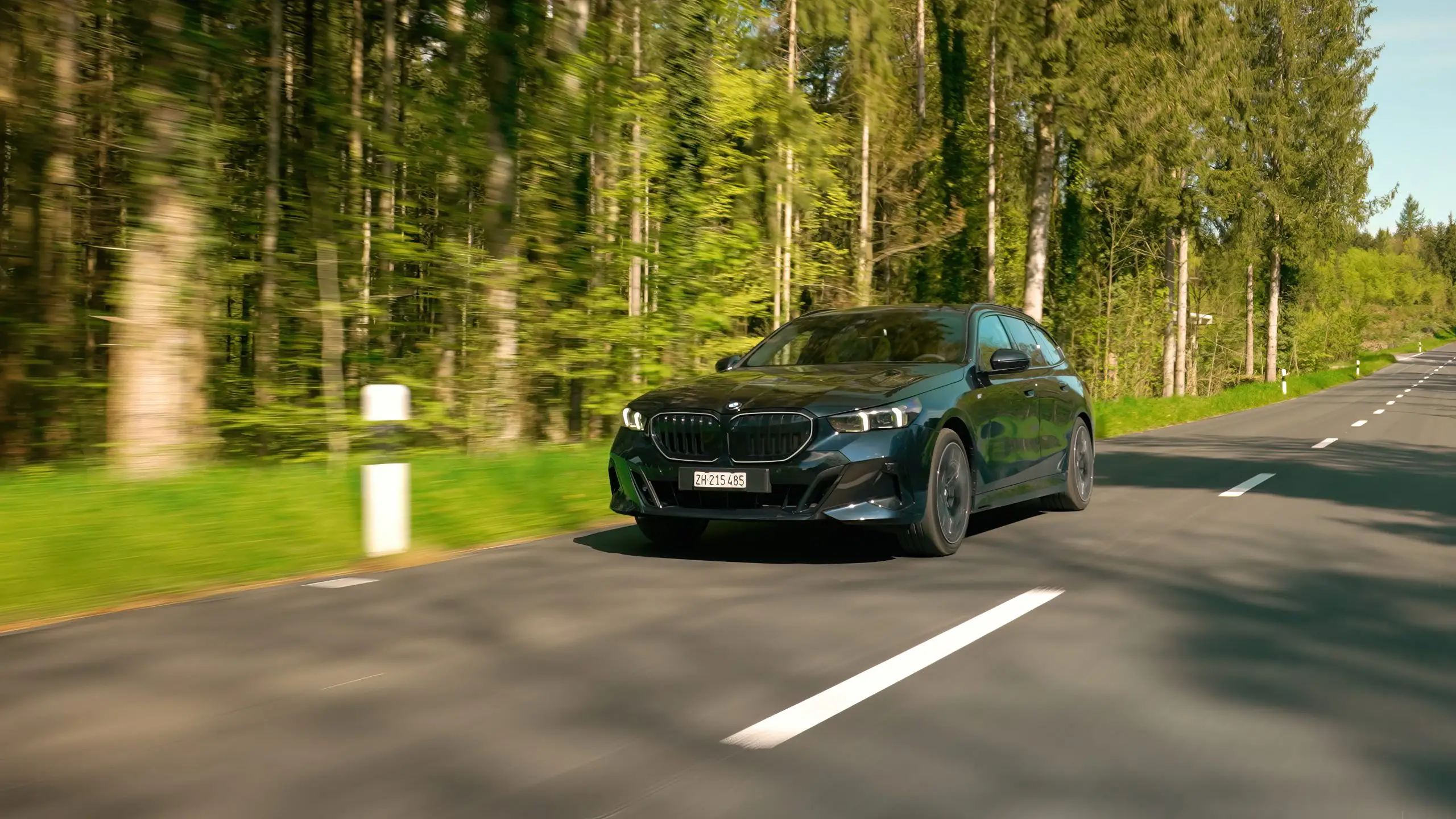 Dunkler BMW 540d Touring fährt auf einer Landstrasse durch einen Wald.