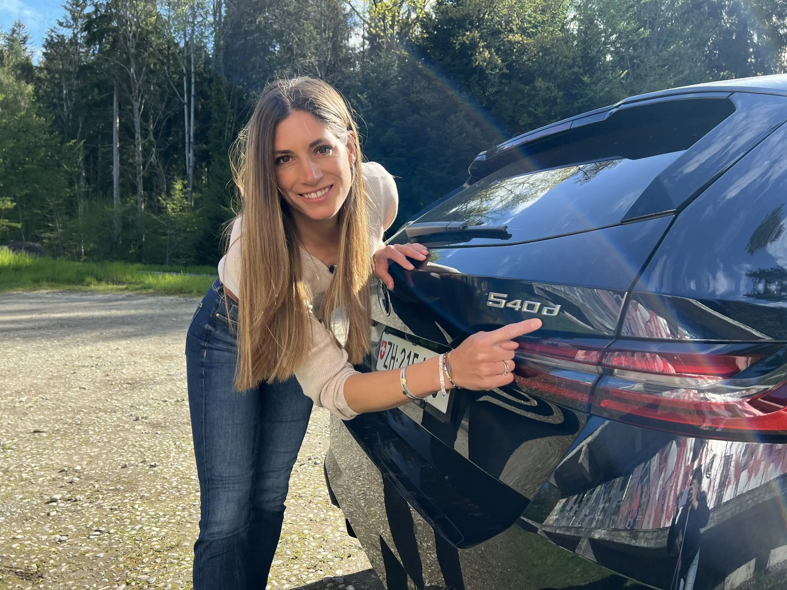 Cyndie Allemann zeigt auf das 540d-Emblem am Heck des schwarzen BMW-Kombis.