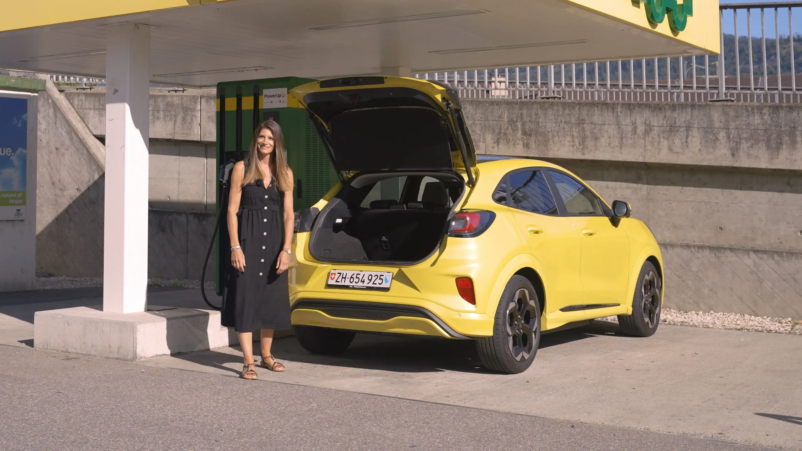 Cyndie Allemann neben dem gelben Ford Puma Gen-E mit geöffneter Heckklappe an einer Ladestation