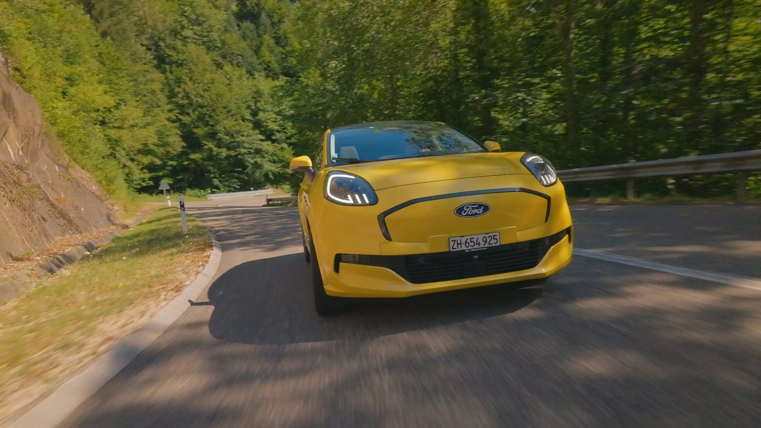 Ford Puma Gen-E fährt durch eine Kurve auf einer bewaldeten Landstrasse