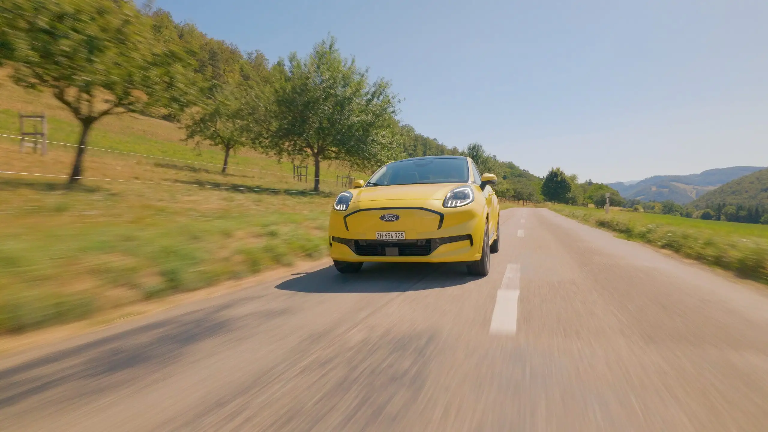 Gelber Ford Puma Gen-E fährt auf einer Landstrasse durch eine hügelige Landschaft