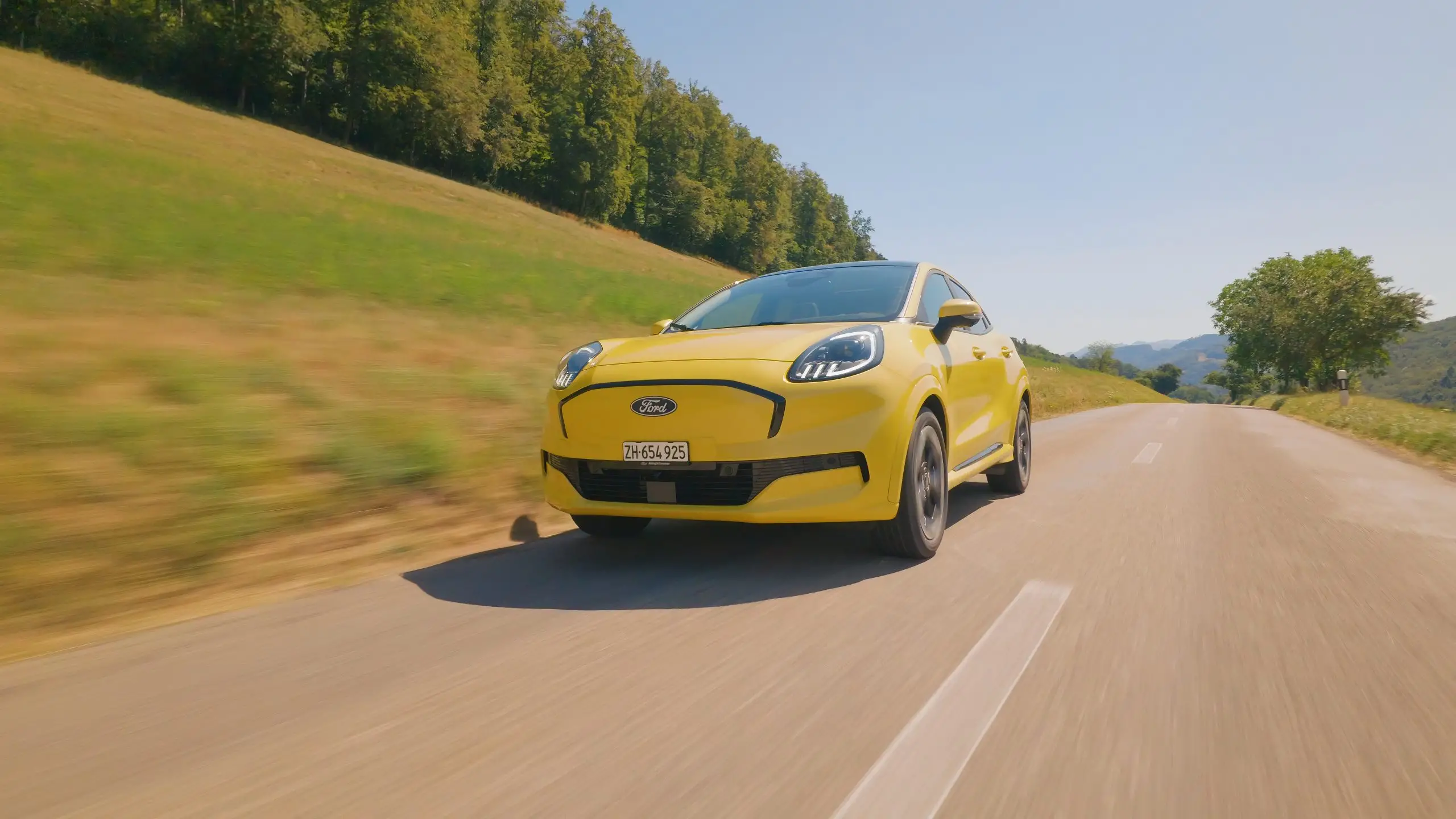 Gelber Ford Puma Gen-E fährt an Wiesen und Bäumen vorbei