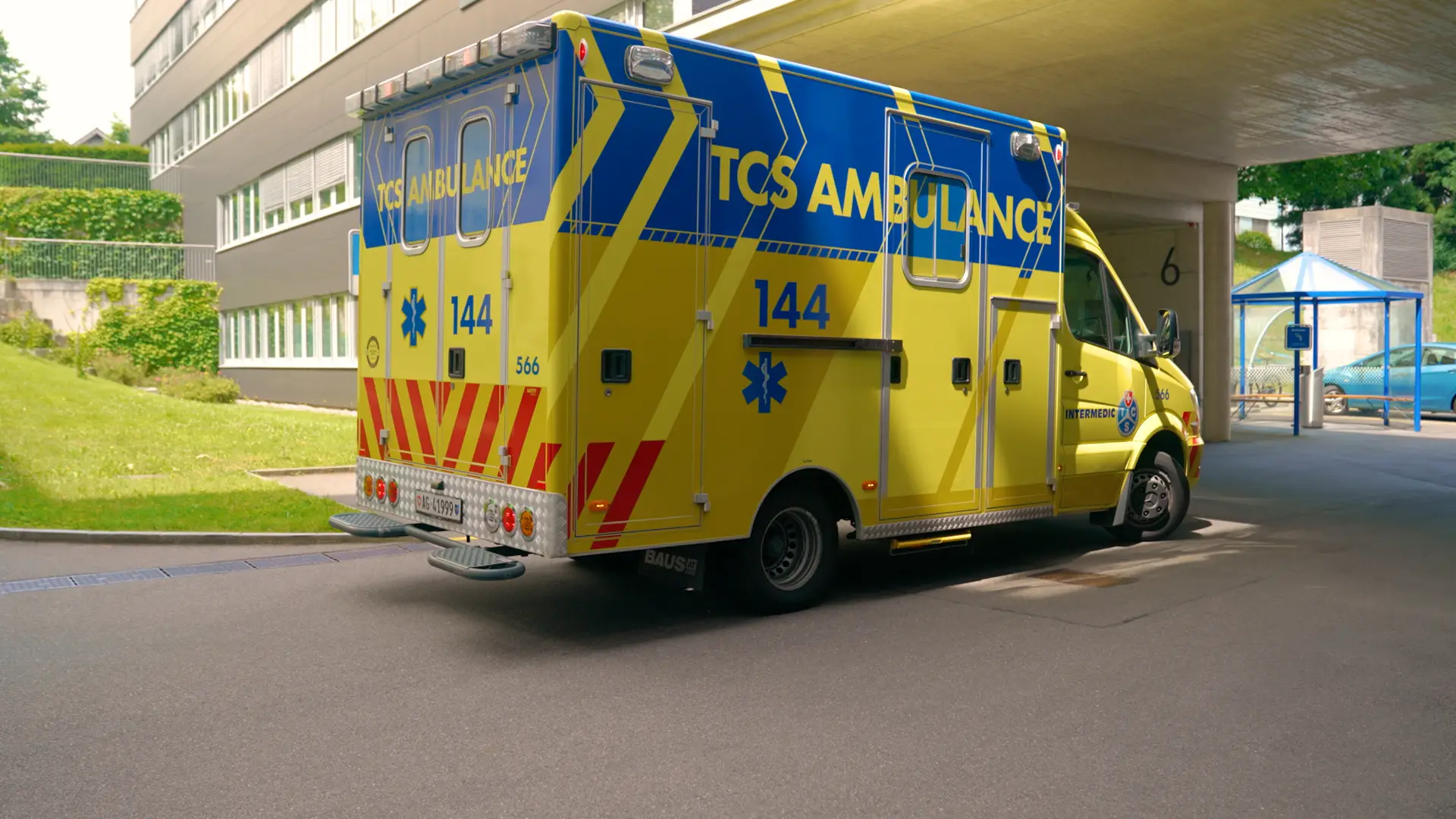 Gelb-blaue TCS-Ambulanz steht vor einem Gebäude, von hinten und der Seite sichtbar.