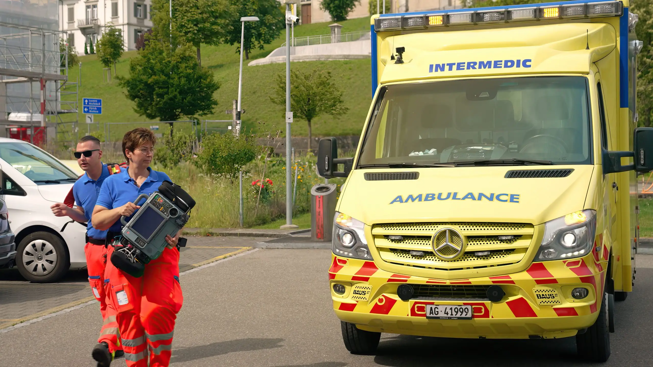 Zwei Rettungssanitäter gehen mit Notfallausrüstung zur gelben Ambulanz am Strassenrand.