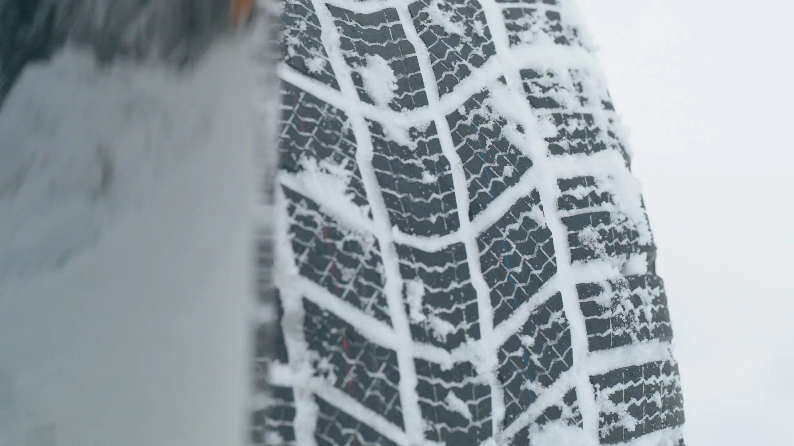 Nahaufnahme eines Winterreifenprofils mit Lamellen und Schnee in den Profilrillen.