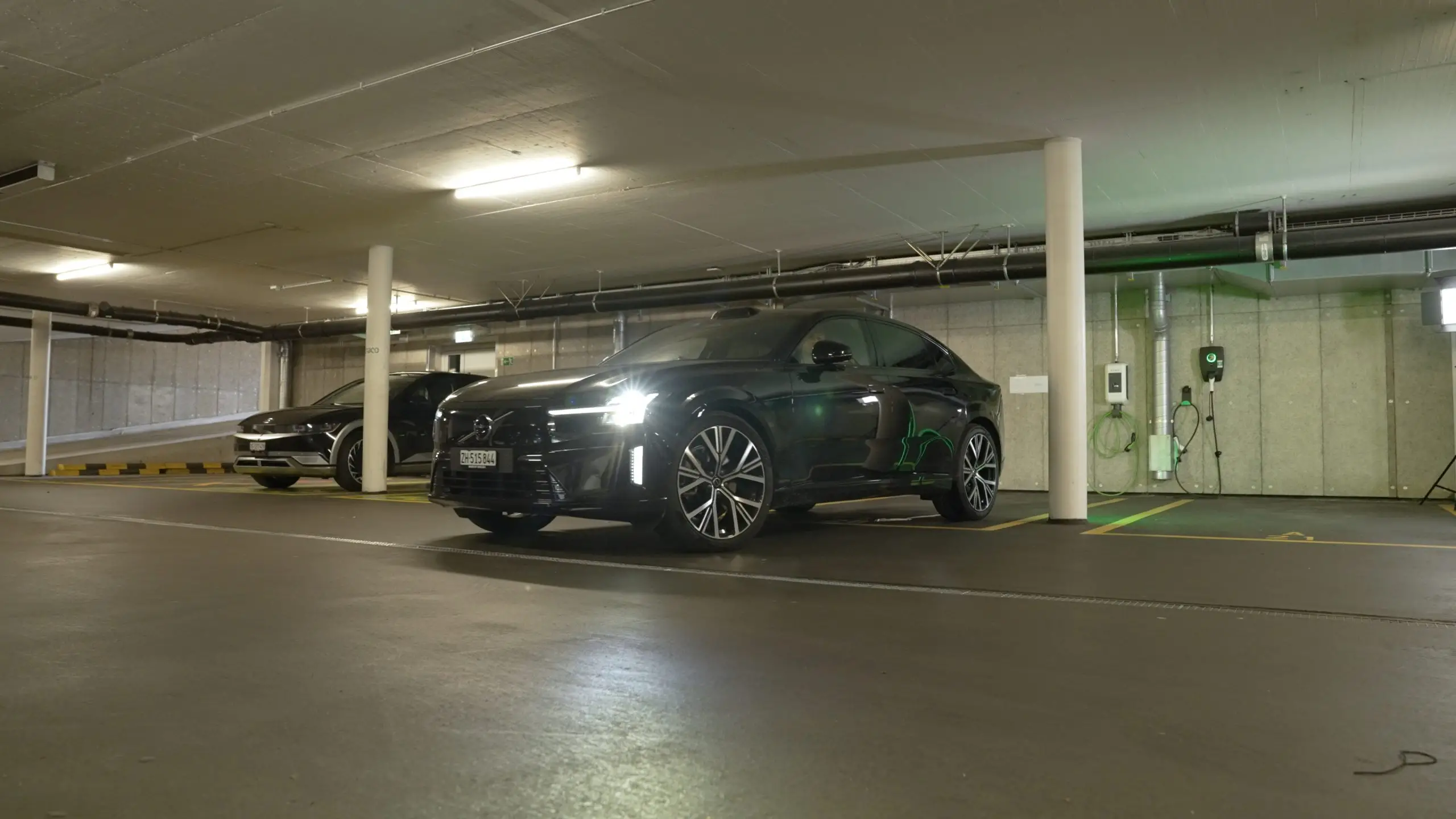 Dunkles Elektroauto neben zwei Wallboxen an einer Betonwand in einer Tiefgarage.